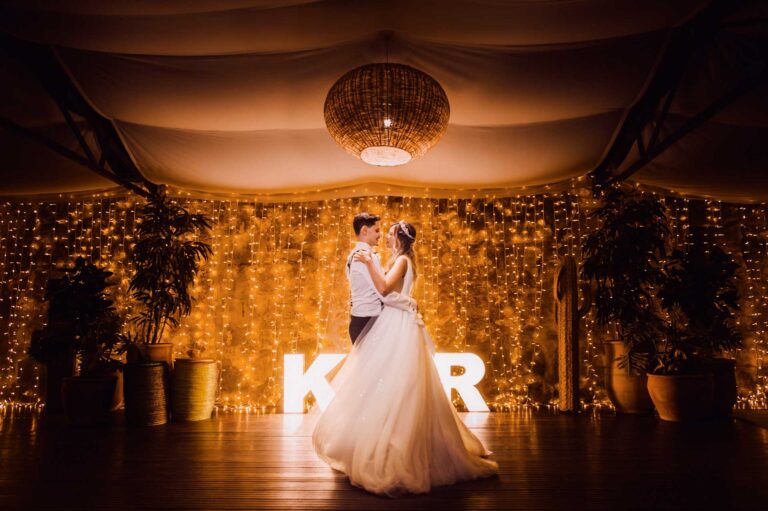 Pár novomanželů tančí na svatbě s pozadím zlatých světel a svítících písmen K a R.